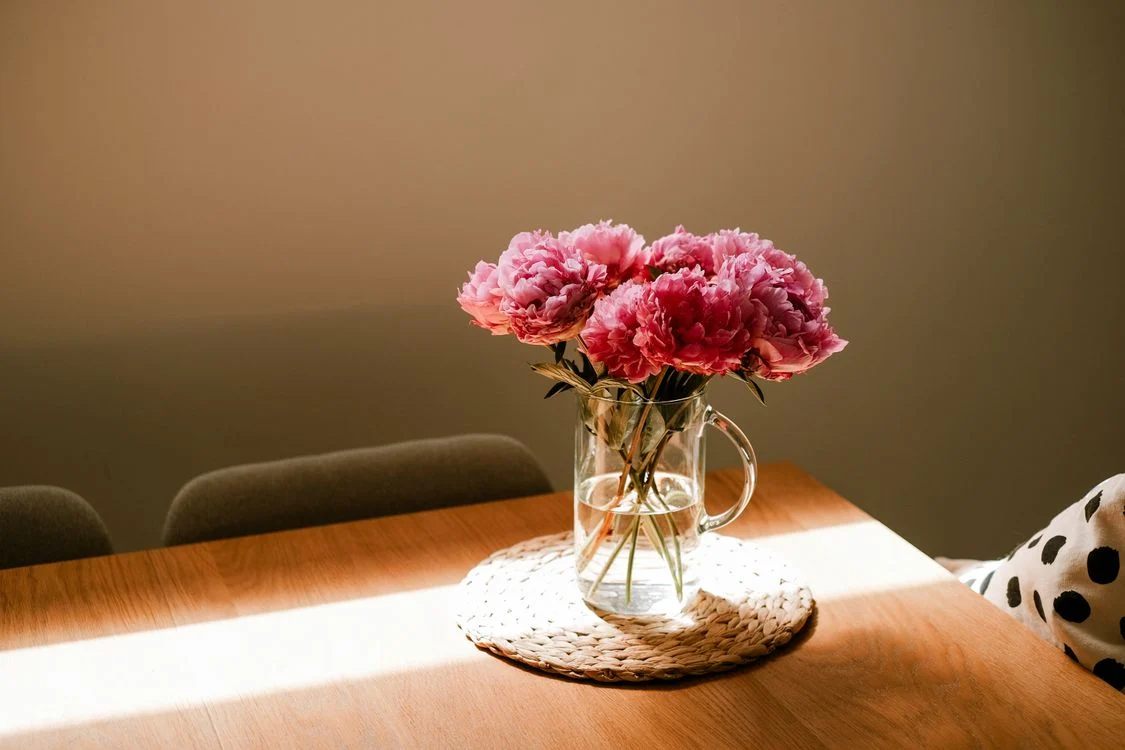 Pink peonies in a glass jug on a sunlit table
